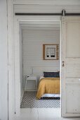 Open sliding door and view of bed in simple bedroom with white wooden wall