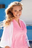 Junge blonde Frau in rosa Bluse und weisser Strickjacke