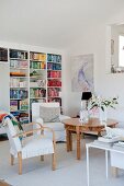 Armchairs at round wooden table with carved legs and bookcase in modern living area