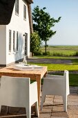 Moderne Outdoor-Stühle aus weißem Kunststoff und Holztisch auf sommerlicher Terrasse vor Ferienhaus