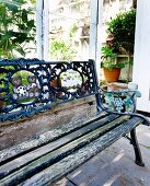 Vintage garden bench with peeling paint and ornate cast iron backrest outside greenhouse
