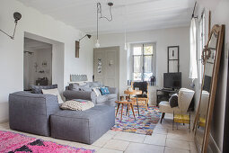 Grey armchair with matching stool and retro armchair around side tables in living area in patterned rug on tiled floor