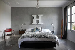 Felldecke auf Bett vor grauer Stuccolustrowand mit weißem Deko-Buchstabe
