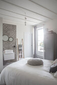 Bett mit weisser Tagesdecke und Waschtisch vor gefliester Wand mit grauen Ornamentfliesen in restauriertem Schlafzimmer