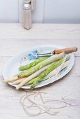 Green and white asparagus with a peeler and peelings on a porcelain plate