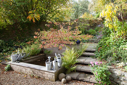 Watering cans on edge of pond and steps in autumnal garden