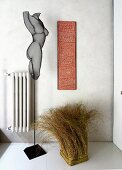 Metal sculpture and bundle of grass next to artwork and radiator on wall