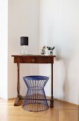 Blue wire stool at antique writing desk in corner of minimalist living room