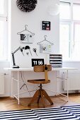 Vintage wooden swivel chair and white desk with classic metal frame below scissors and magazines on coathangers hung on wall