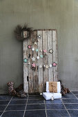 DIY-Girlande aus Häkeldeckchen und Weihnachtskugeln an Bretterwand, Zapfen und Geschenke auf dem Boden