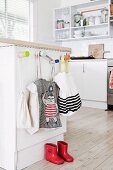 Children's wardrobe at kitchen counter with fabric bags and red children's rubber boots on plank floor