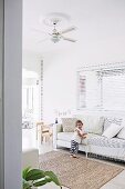 Little girl on bright upholstered sofa in living room with children's play area and colorful garland
