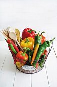 Colourful peppers and a wooden spoon in a wire basket