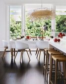 White kitchen counter with wicker bar stools in front of a set dining table and garden view
