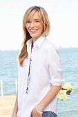 A young blonde woman by the sea wearing a white blouse and jeans