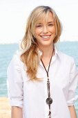 A young blonde woman by the sea wearing a white blouse and jeans