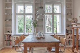 Retro cantilever chairs around wooden table below pendant lamps and custom open-fronted shelves either side of and between windows in dining room