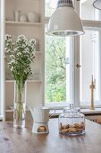 Teapot on warmer, vase of flowers and glass biscuit jar on wooden table