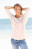 A blonde woman by the sea wearing a white shirt and jeans