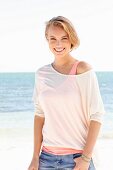 A blonde woman by the sea wearing two tops and jeans