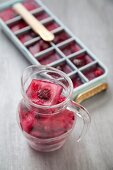 Berry ice cubes in an ice cube tray and in a glass jug