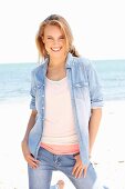 A young woman wearing tops, a denim shirt and jeans on a beach