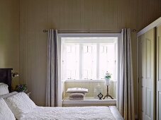 View over double bed with white bedspread in wooden bedroom to window niche