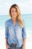 A young woman by the sea wearing jeans and a denim shirt
