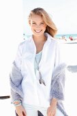 A blonde woman on a beach wearing a white blouse and a purple cardigan