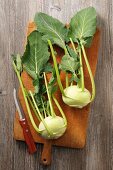 Two fresh kohlrabi on a wooden chopping board (seen from above)