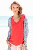 A blonde woman on a beach wearing a red top and a cardigan