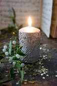 Lit candle with silver snowflake structure next to sprig of mistletoe