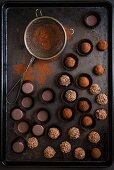 Various chocolate truffles with a sieve and cocoa powder on a baking tray