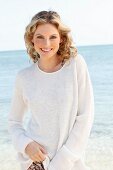A young woman on a beach wearing a white knitted jumper