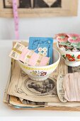 Old sewing utensils in bowl with floral motif on stack of papers