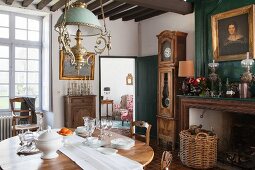 Ovaler Holztisch mit Porzellangeschirr in traditionellem Esszimmer mit antiker Standuhr und Ölgemälden