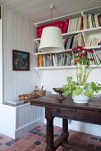 Flowering potted plant on antique console table below bookshelves on white wooden wall