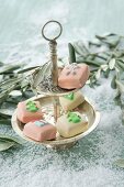 Christmas petit fours decorated with marzipan between olive sprigs on the table covered with snow