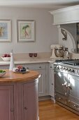 Panelled cabinets, pastel colour scheme, island counter and vintage-style cooker in rustic kitchen