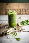 A glass of kiwi and spinach smoothie with fresh spinach leaves and slices of kiwi