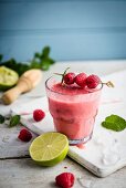 A glass of smoothie garnished with fresh raspberries and mint