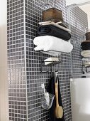 Stacked towels on top of wall-mounted shelves with hooks below on grey mosaic-tiled wall