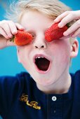 A boy holding two strawberries in front of his eyes
