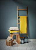Holzleiter als Kleiderständer mit gelbem Tuch, Kissenstapel auf Holzhocker