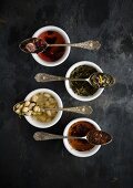 Vier Vintage-Löffel mit verschiedenen Teesorten auf Teeschalen (Draufsicht)