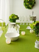 Stack of crockery, glasses and lanterns on green set table with flower decoration