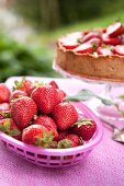 A basket of fresh strawberries with a strawberry cake in the background
