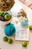 Christmas arrangement of green apples, turquoise felt flower, hellebore flowers and drawing on piece of wood on table