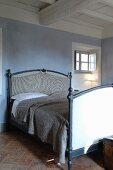Double bed against blue-grey wall below white-painted wood-beamed ceiling