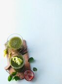 Two green smoothies garnished with golden rod and lettuce